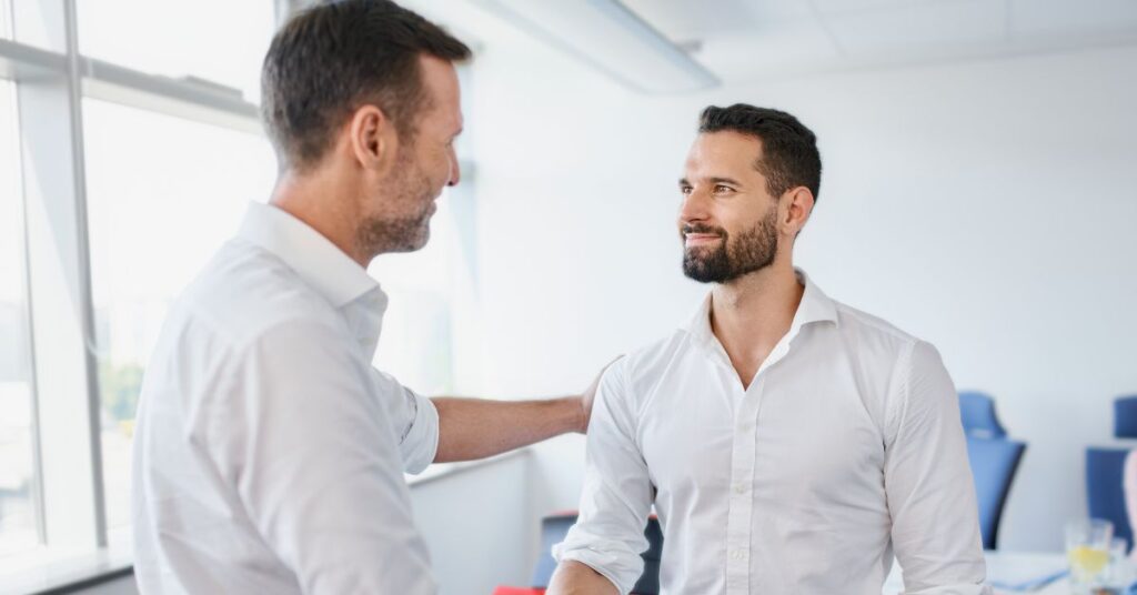 Two professionals greet each other with a handshake and a smile in a bright office, capturing a positive onboarding moment.