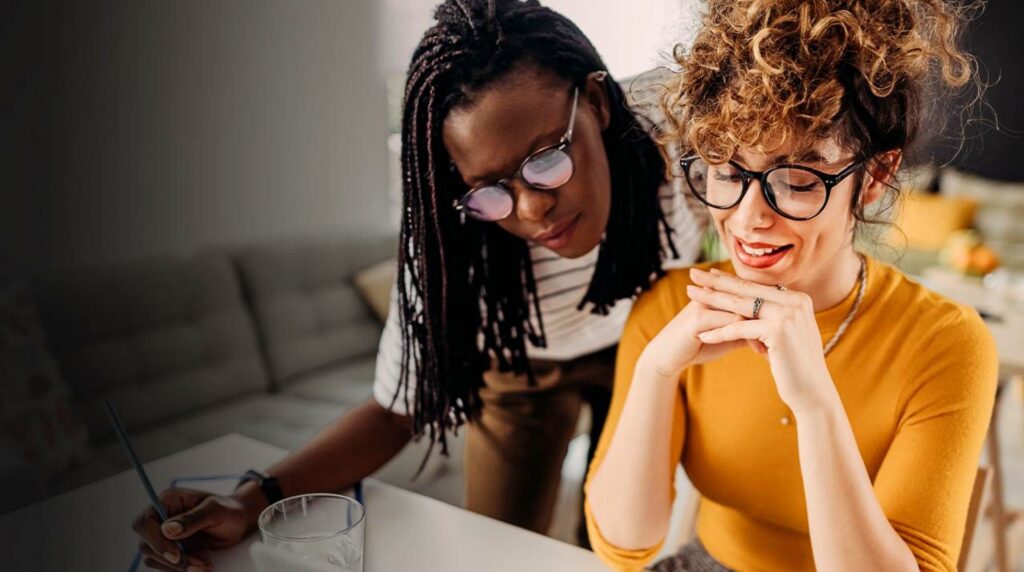 Two female professionals collaborating and reviewing notes together in a modern workspace.