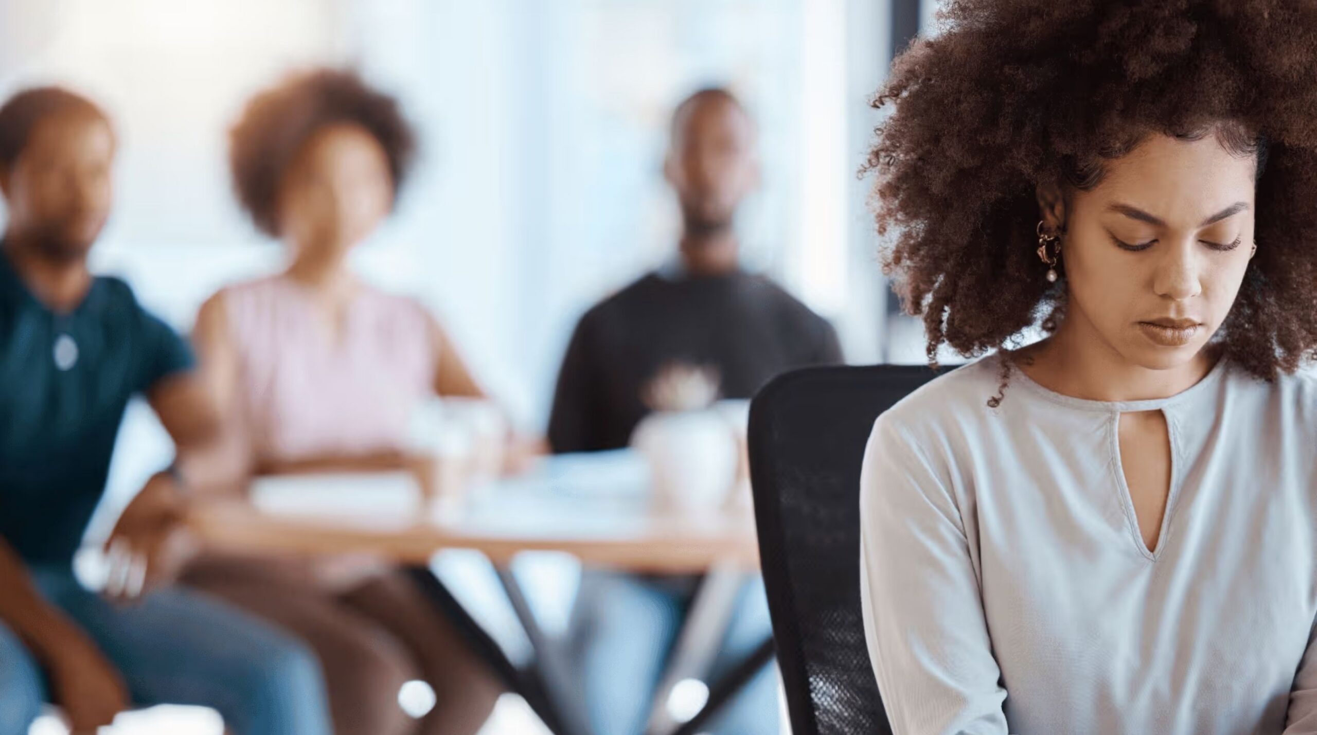 Employee sitting apart from team during a meeting, highlighting workplace exclusion and the importance of a safe and respectful work environment.